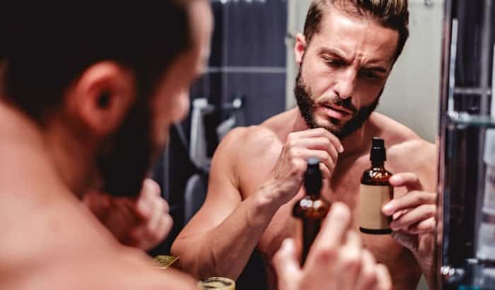 man staring at a bottle of beard growth spray